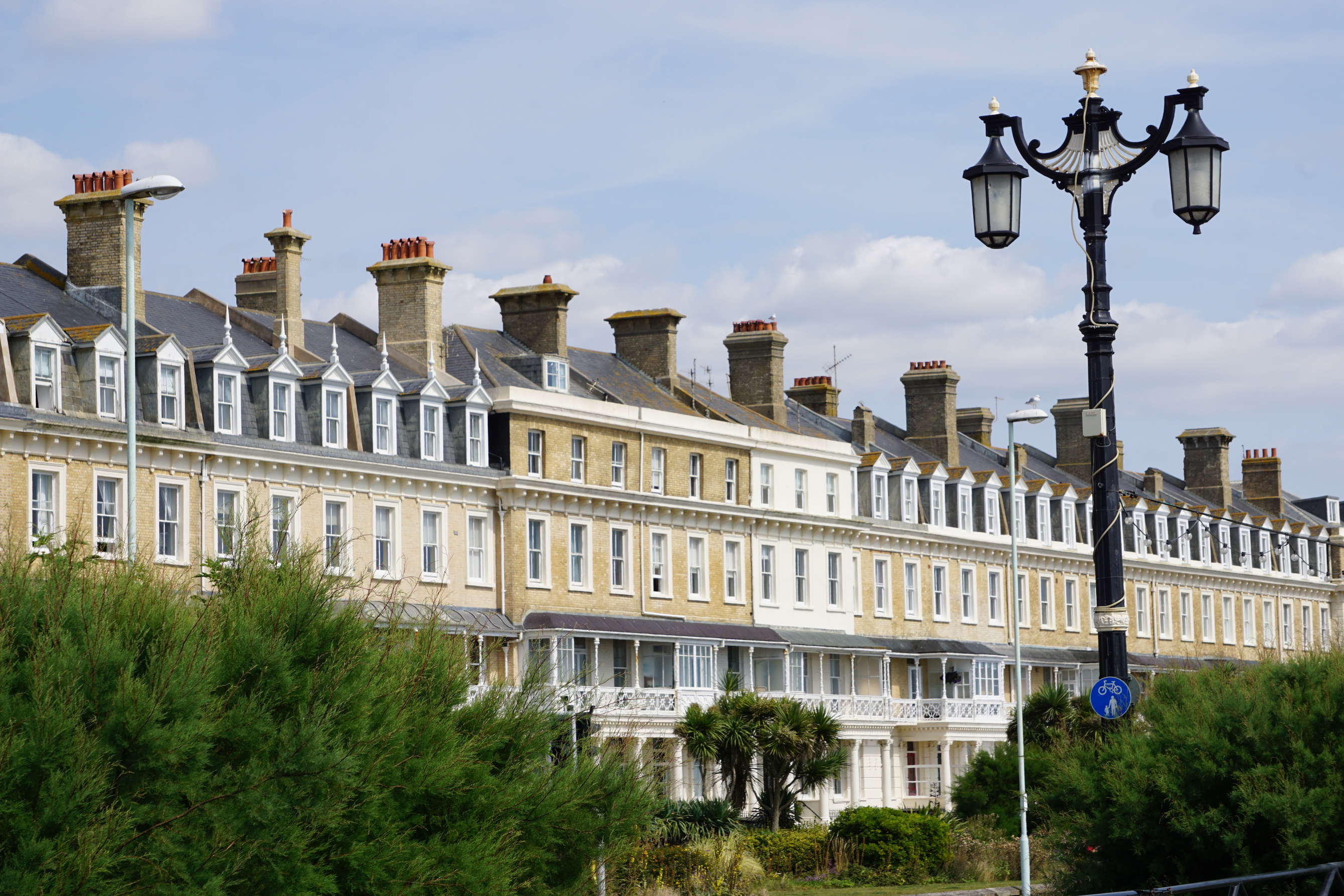 a_row_of_traditional_terraced_houses_with_bay_windows_and_balconies_overlooking_a_green_area_with_lush_foliage_and_a_lamppost_in_worthing_in_the_uk_england
