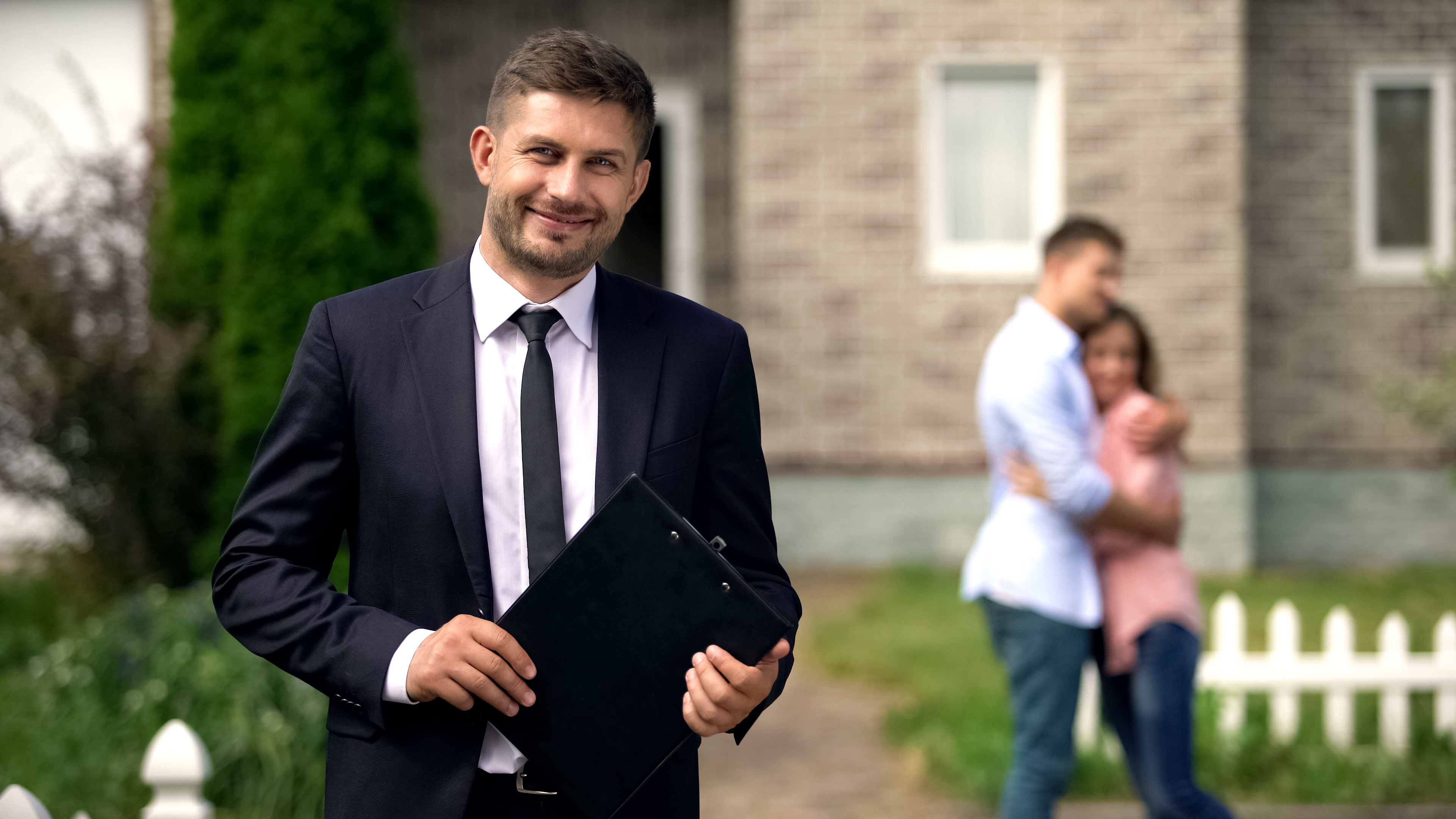 estate agent with happy family hugging near their new home