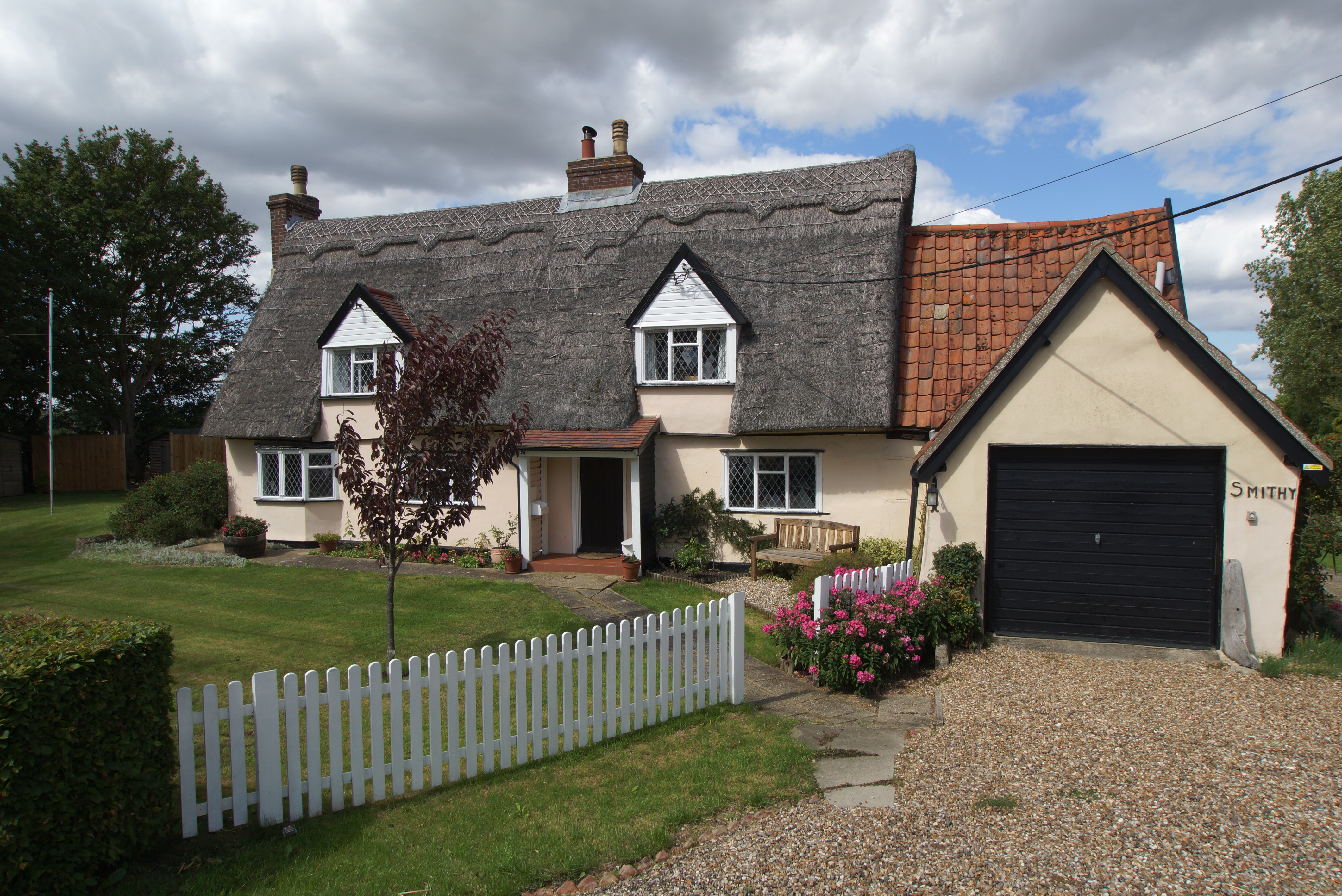 Grade II Lised thatched cottage with white picket fence and flowers