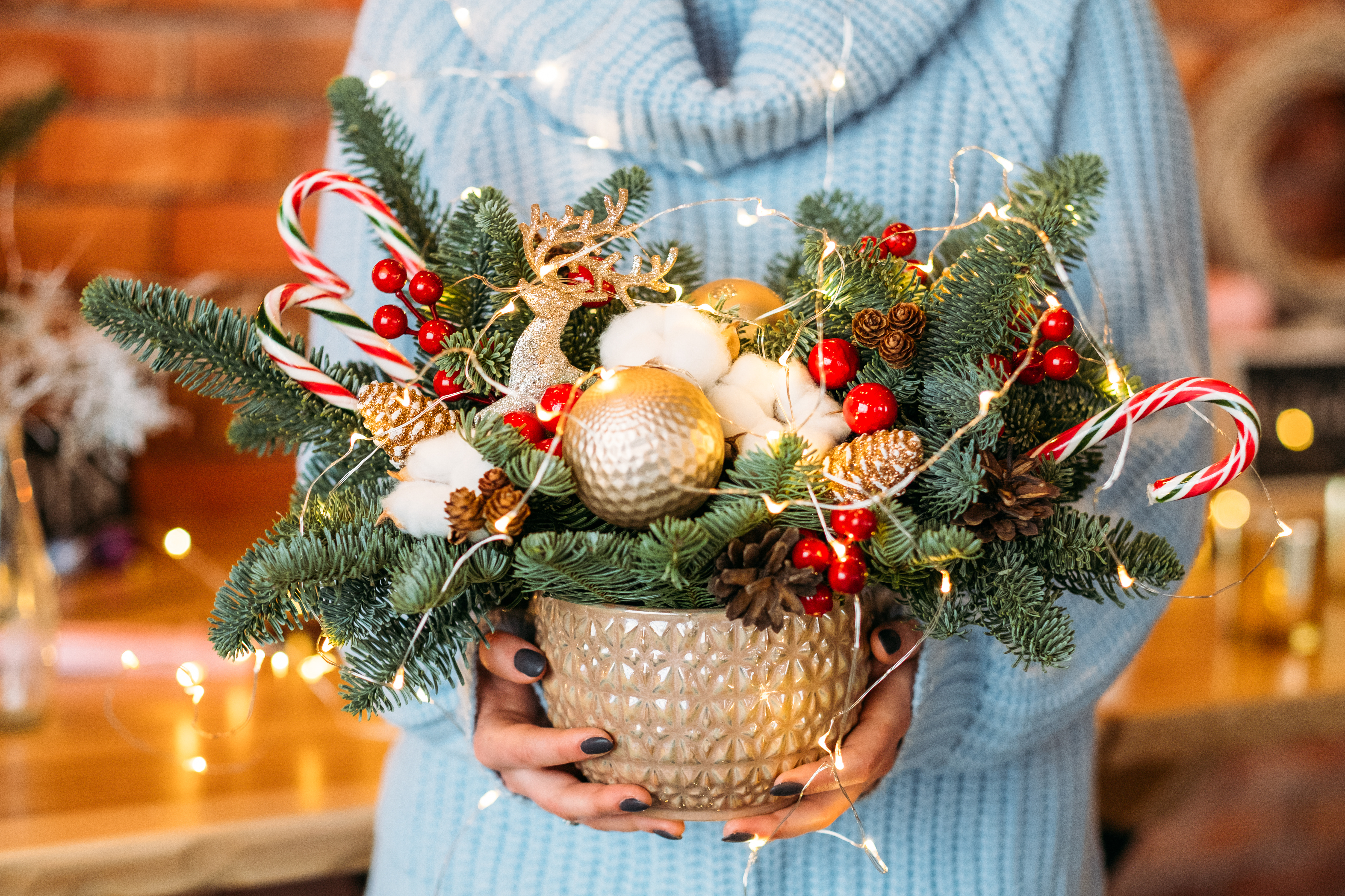 Handmade Christmas decor. Cropped shot of lady holding pot with fir tree twigs, candy canes and fairy lights.