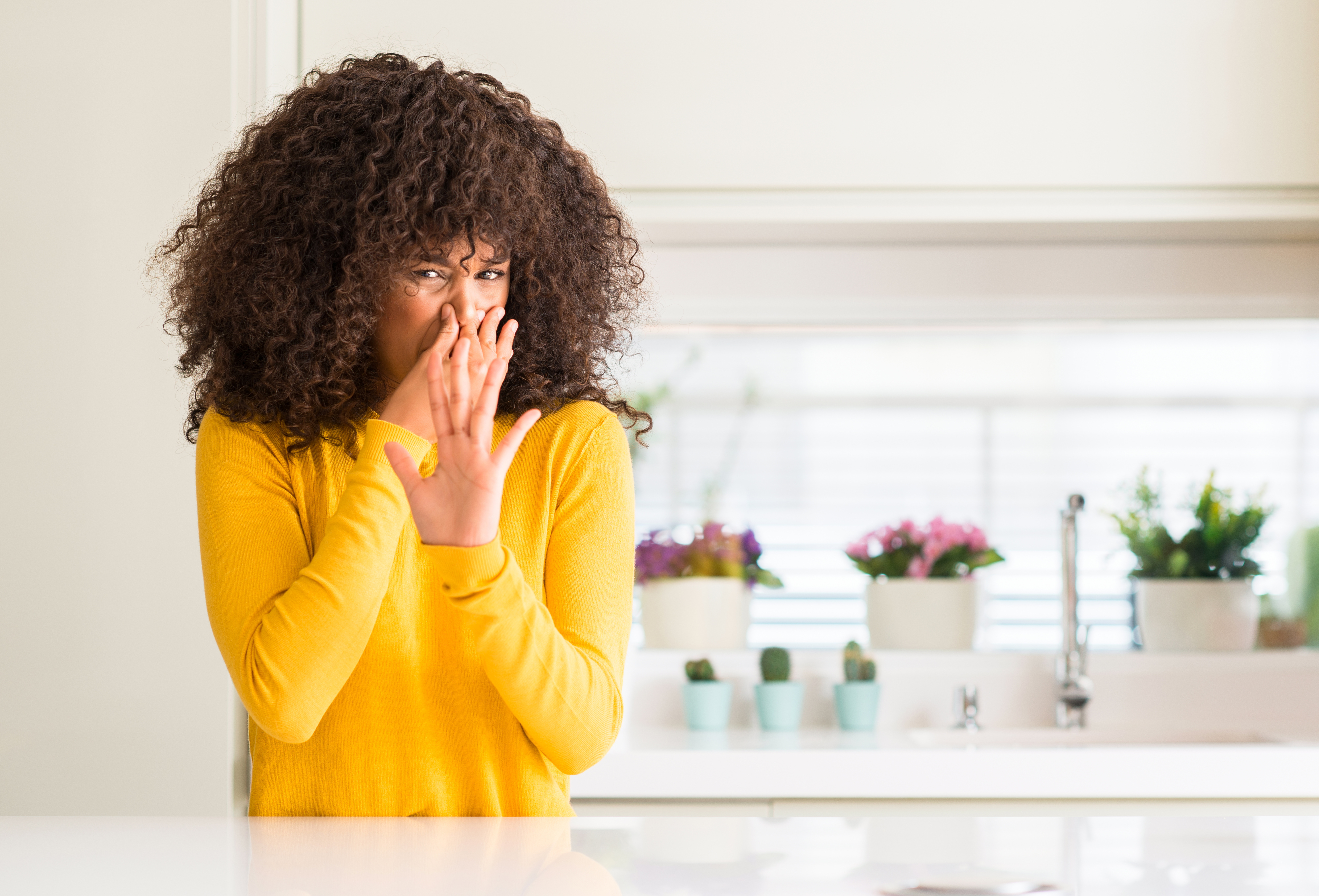 woman wearing yellow sweater at kitchen smelling something 