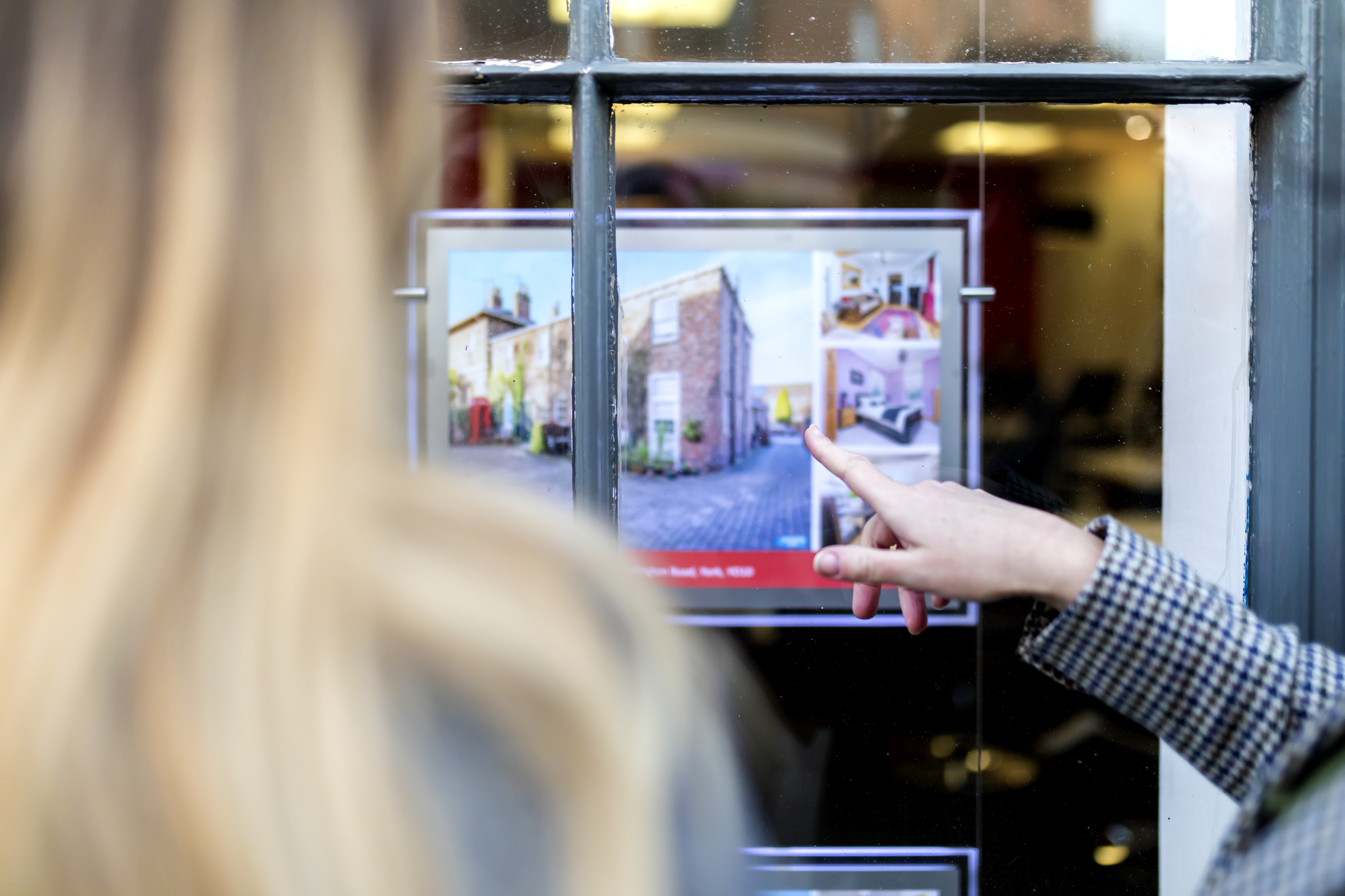 Couple looking at a property advert in the window of an estate agents or real estate shop window in England