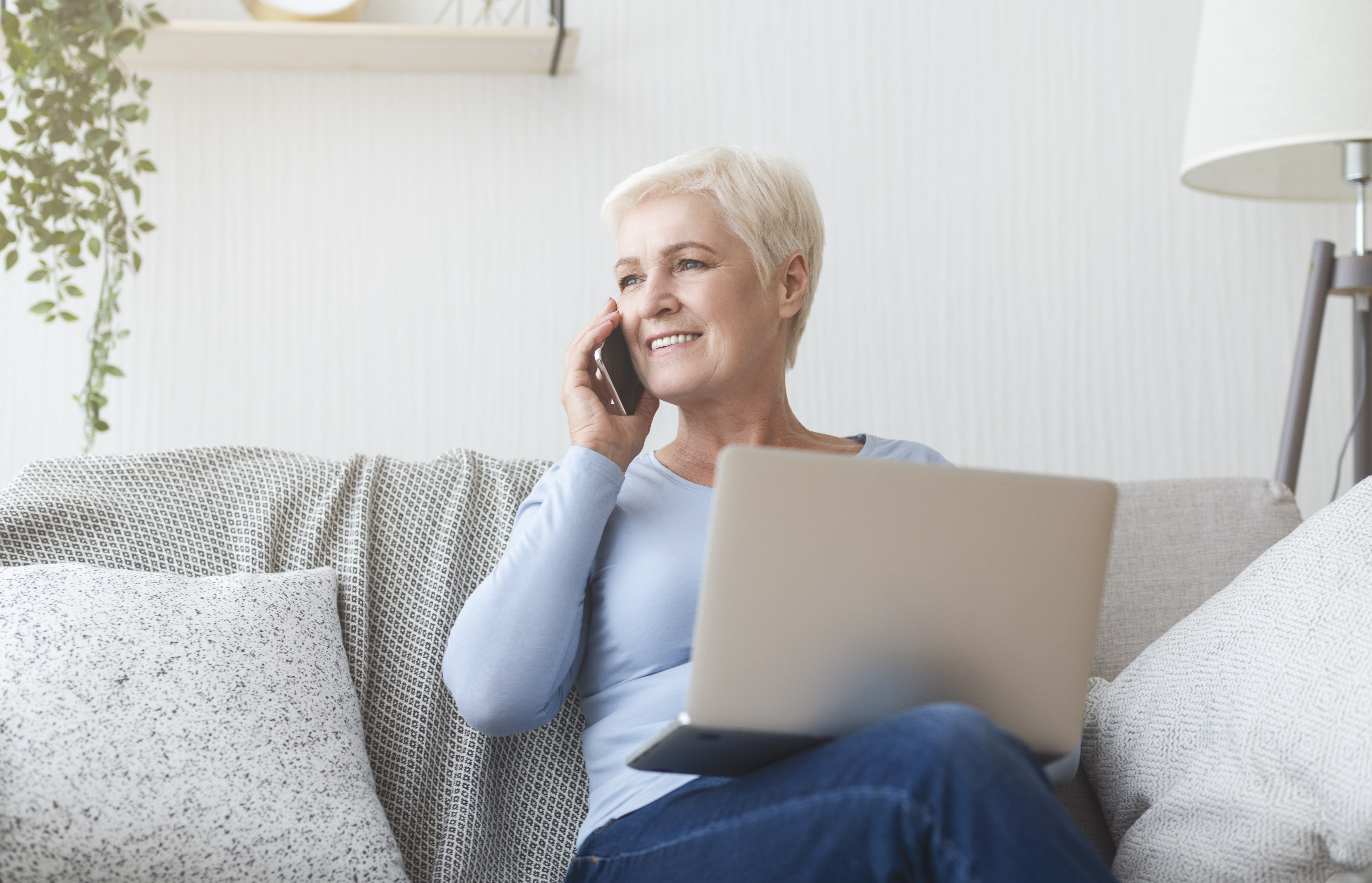 Modern senior woman holding laptop and talking by phone